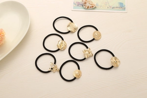 Close-up of seven black high-elastic hair ties with various golden alloy charms on wood