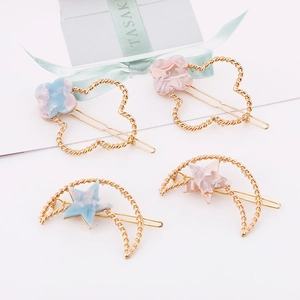 Détail de quatre barrettes en métal doré avec motifs trèfle et lune en marbre rose