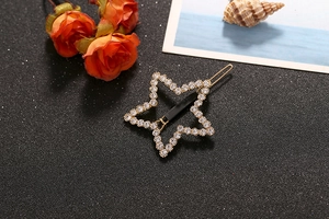 Detailed view of a gold-plated star hair clip with crystals on a textured black surface