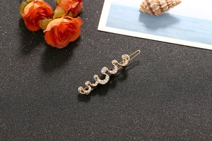 Macro shot of wavy gold-plated hair clip with sparkling white rhinestones on dark surface