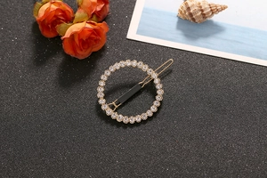Close-up of a circular gold-plated hair clip set with sparkling white rhinestones