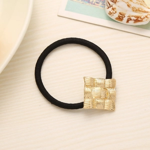 Elastic hair tie with a textured golden square charm on a minimalist flat lay background