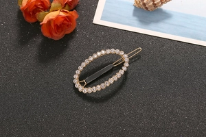 Detail of oval gold-plated hair clip with sparkling white rhinestones on dark background