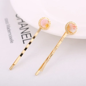 Close-up of golden alloy hair clips with pink marble resin circles on a white ceramic plate