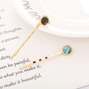 Detail of golden alloy hair clips with circular cat-eye stone decorations on a white plate