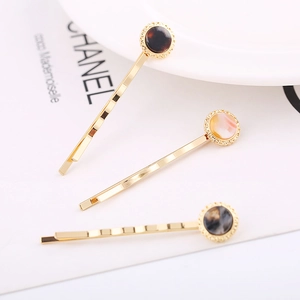 Detailed view of three gold alloy hair clips featuring round tortoiseshell and resin heads