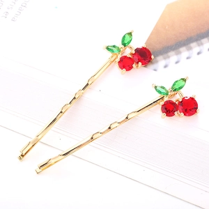 Détail de deux barrettes dorées avec motifs de cerises en zircone rouge et verte de luxe