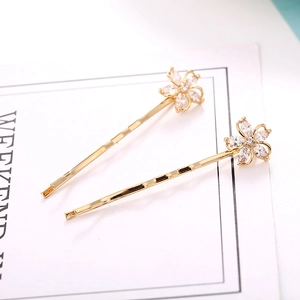 Detail of gold metal hair clips featuring sparkling flower-shaped zircons on white card