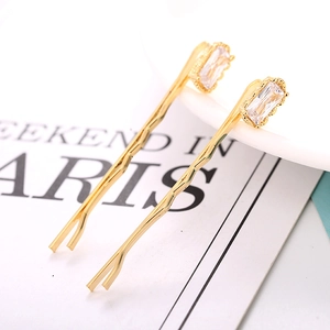 Detailed view of two gold hair clips with rectangular zircon and branch-like texture