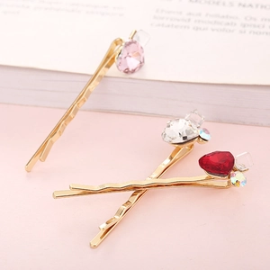 Dettaglio di tre fermagli per capelli in cristallo rosso, rosa e bianco su rosa