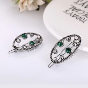 Détail d'un lot de pinces à cheveux vintage avec strass verts et blancs sur métal foncé
