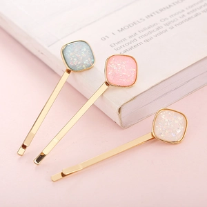 Close-up of three gold-plated hair clips featuring shimmering square resin inlays