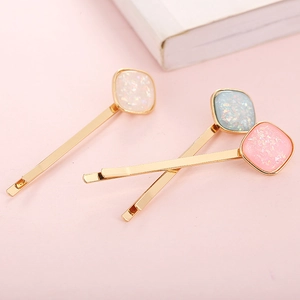Macro detail of three pastel square hair clips with glitter texture on gold plating