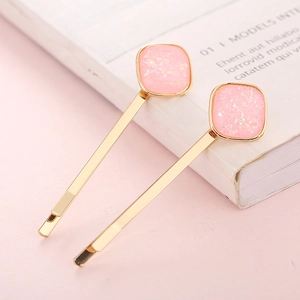 Pair of golden hairpins with pink glitter resin squares on pink aesthetic background