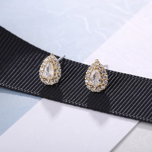 Macro shot of gold teardrop stud earrings with halo diamonds on black silk ribbon