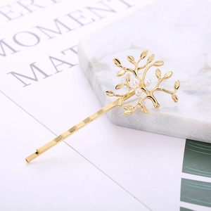 Détail de la barrette à cheveux dorée en forme de branche avec perles sur marbre chic