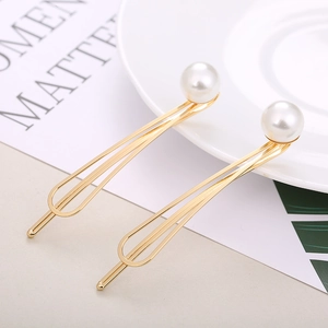 Vue détaillée de deux pinces à cheveux dorées avec perles blanches sur une assiette