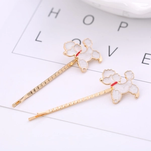 Detail of two gold metal hair pins with cute white enamel dog charms on white card