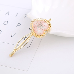 Detailaufnahme einer goldenen Haarklammer in Herzform mit echten rosa Trockenblumen