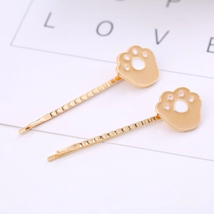 Detail view of two gold cat paw hair clips with white enamel on a gift card display