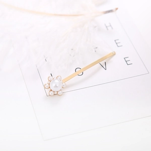 Elegant gold metal hair clip with white pearl flower design on a minimalist white background