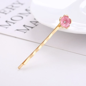 Gros plan détaillé d'une pince à cheveux fleur de cerisier dorée avec émail rose et strass
