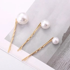 Detailed view of three golden hair clips with graduated white pearls on a grey background