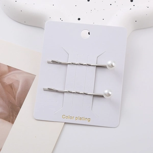 Detail view of silver wave patterned hairpins with white pearls on a display card
