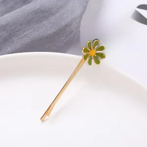 Close-up of a gold daisy hair clip with green enamel petals on a ceramic dish