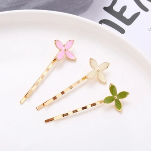 Three gold-plated alloy hair clips with colorful enamel clover designs in pink white and green