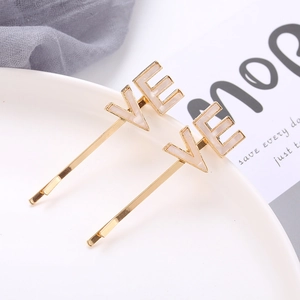 Creative acetate LOVE letter hair clips in gold alloy finish on a white ceramic dish