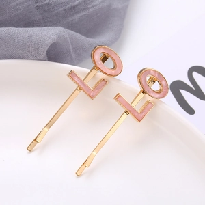 Detail view of gold metal hair clips with pink LOVE letters on a ceramic plate