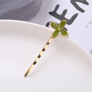 Macro shot of a golden wave hair clip featuring a green four-leaf clover floral motif