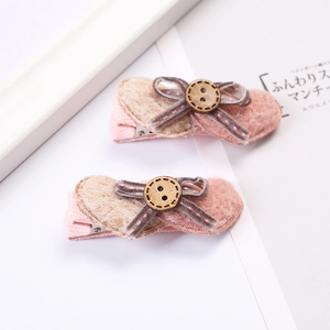 Détail de barrettes à nœuds en feutre rose et avoine avec boutons bois et pinces crocos