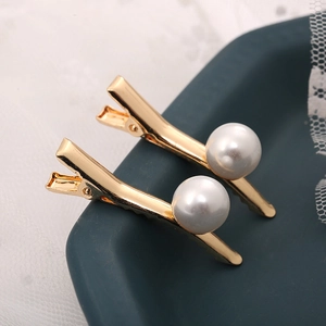 Détail macro de deux pinces à cheveux dorées avec de grandes perles blanches sur plateau