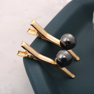 Vue macro de barrettes dorées avec perles gris foncé sur un plateau en céramique