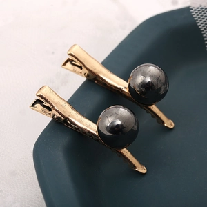 Barrettes à cheveux dorées ondulées avec sphères gris foncé sur un plateau élégant