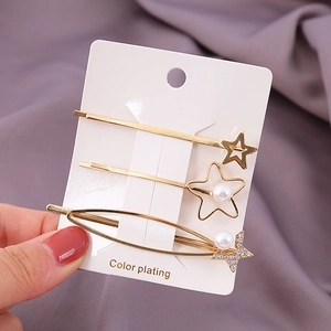 Dreiteiliges Set goldener Haarspangen mit Sternen und Perlen auf einer weißen Karte