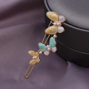 Elegante Schmetterlings-Haarspangen aus Goldlegierung mit Perlen auf lila Seidenstoff
