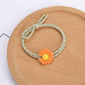 Élastique à cheveux marguerite orange et vert présenté sur un plateau en bois