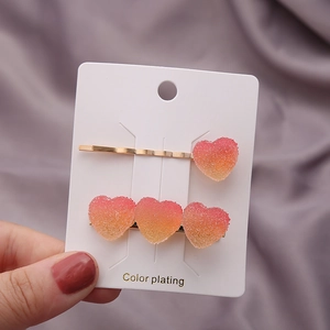 Détail de pinces à cheveux cœur dégradé rose-orange avec texture mate sur métal doré
