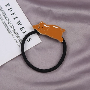 Detailed close-up of a brown bear pendant on a black elastic hair tie with silk backdrop