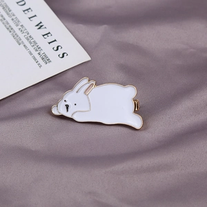 Detailed close-up of a cute white rabbit enamel brooch on a soft satin fabric background