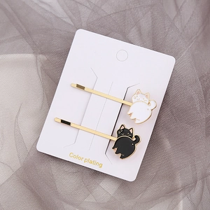 Détail de barrettes chat créatives en finition dorée avec motifs en émail noir et blanc