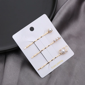 Drei goldene Haarspangen im Set mit weißen Perlen und Herzform auf einer Geschenkkarte