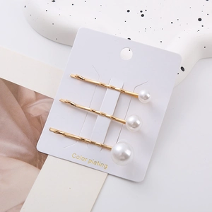Ensemble de trois barrettes dorées avec perles blanches dégradées sur une carte