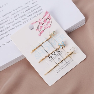 Détail de trois barrettes dorées avec nœuds en émail bleu clair sur carte blanche