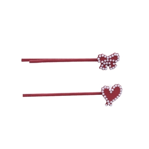 Dettaglio di fermagli rossi a cuore e fiocco decorati con piccole perle bianche