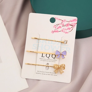 Lot de 3 barrettes dorées avec strass et nœud en émail violet sur carte de présentation