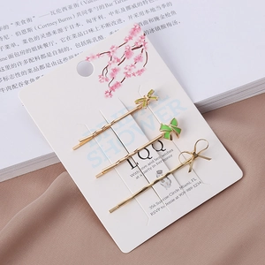 Détail de trois barrettes à nœuds verts en émail et fil doré sur une carte cadeau